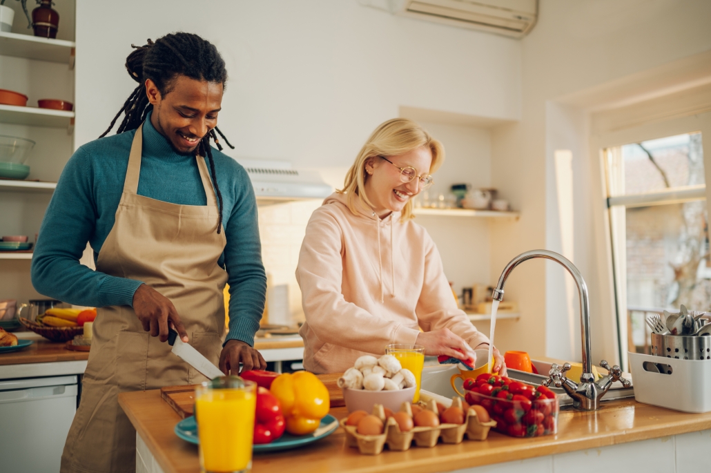 Young couple cooking in modern kitchen with laptop open