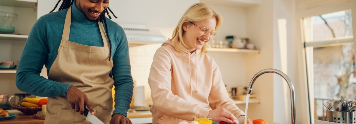 Young couple cooking in modern kitchen with laptop open