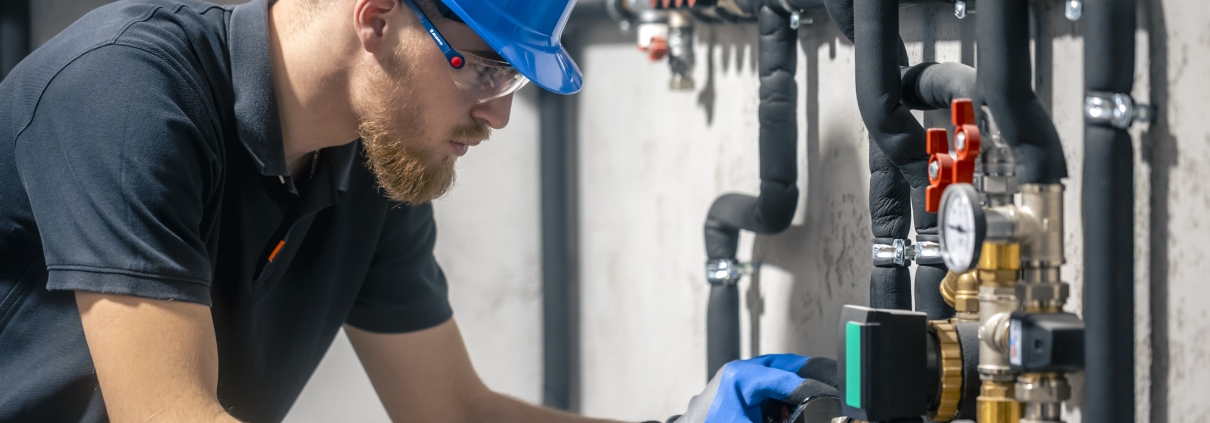 A man installs a heating system in a house and checks the pipes with a wrench.