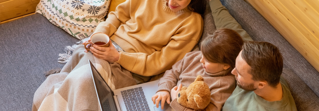 Family sitting on couch using laptop, kids wrapped in blanket