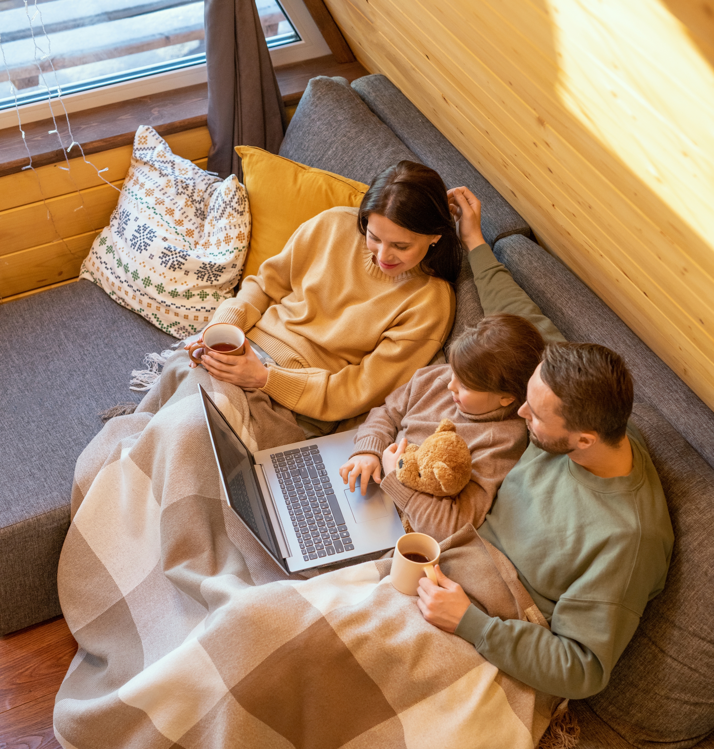 Family sitting on couch using laptop, kids wrapped in blanket