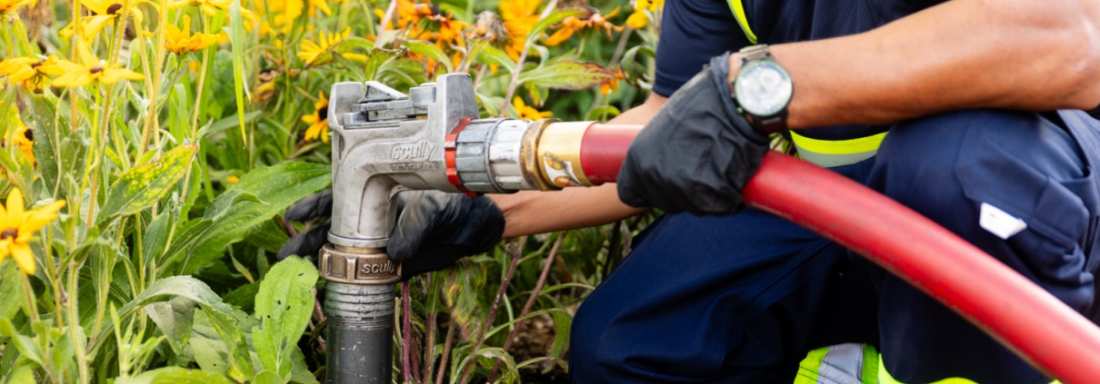 Energo employee connecting a heating oil delivery hose to an outdoor fill pipe beside a flower bed
