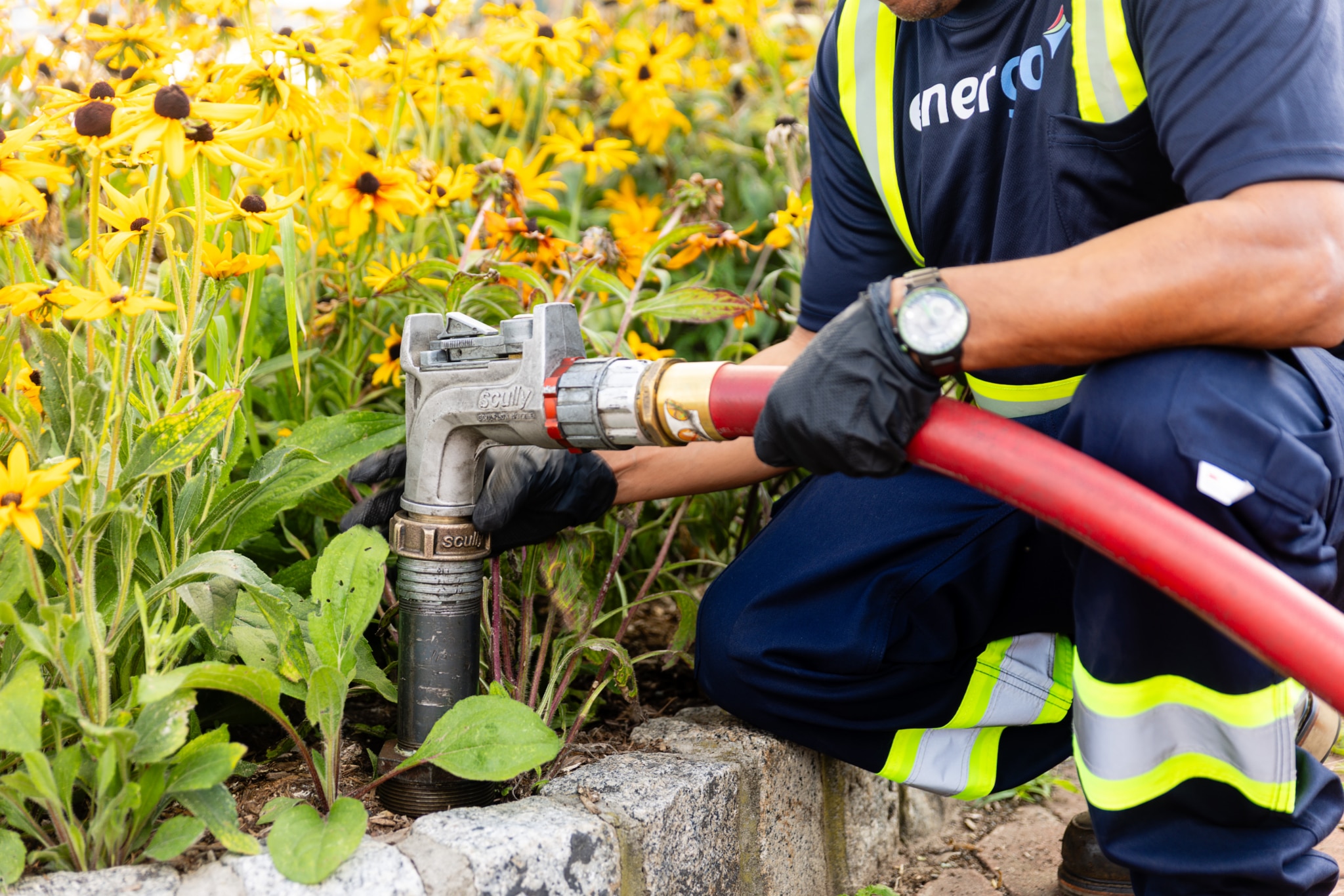 Energo employee connecting a heating oil delivery hose to an outdoor fill pipe beside a flower bed