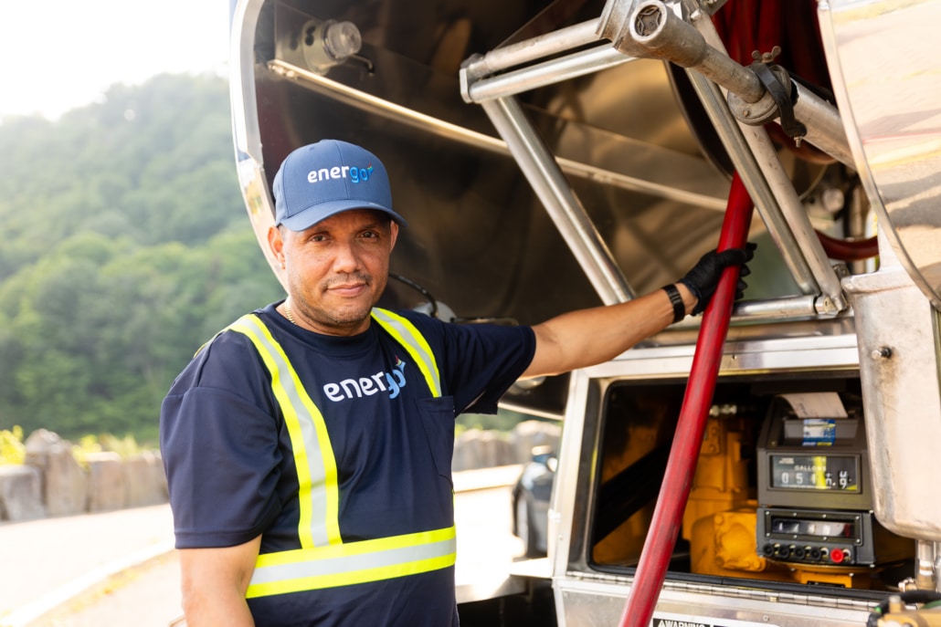 Energo delivery employee holding a red fuel hose beside the tanker meter and controls